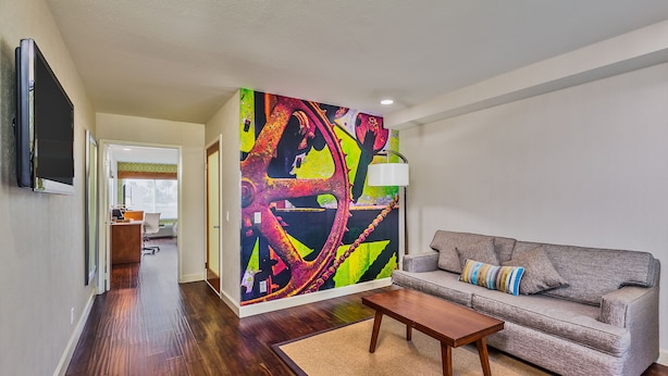 A modern living room with a grey sofa, a wooden coffee table, and a colorful abstract wall mural.