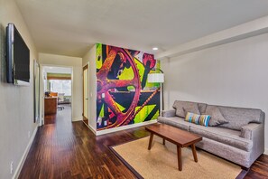 Un soggiorno moderno con un divano grigio, un tavolino in legno e un vivace murale astratto.