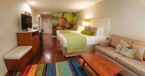 Una camera d'hotel con un letto, un divano, una TV, una scrivania e un tappeto colorato a righe.