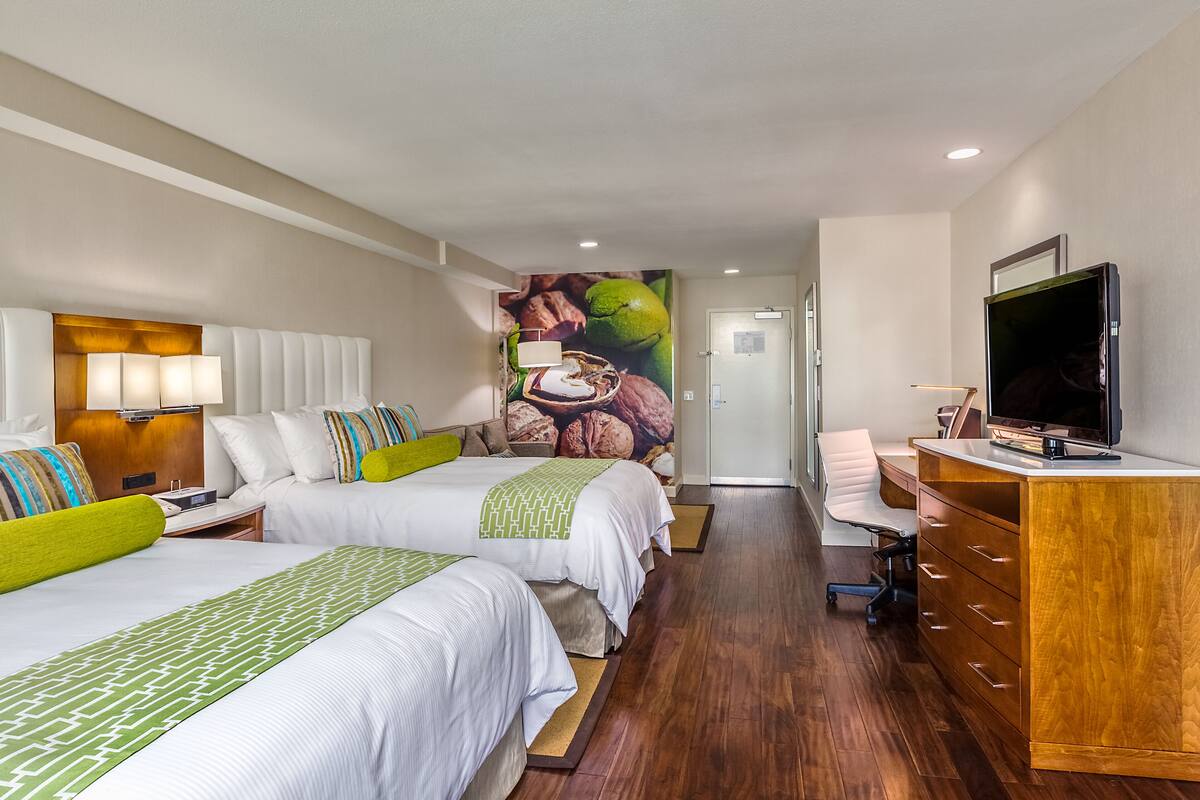A hotel room with two beds, a desk, a television, and a mural on the wall.