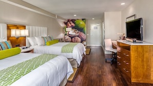A hotel room with two beds, a desk, a television, and a mural on the wall.