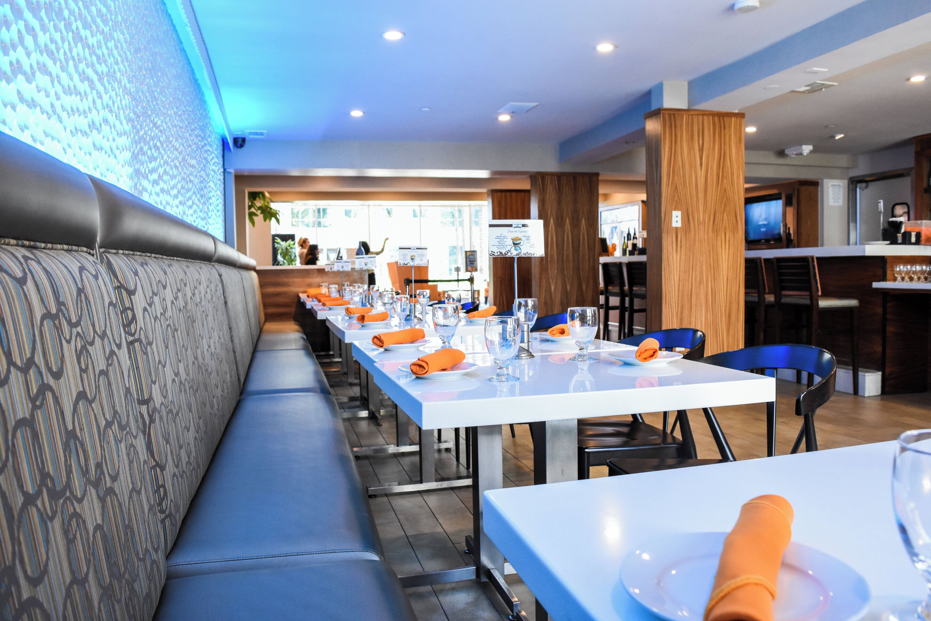 A restaurant with a long counter, blue chairs, and a patterned bench.