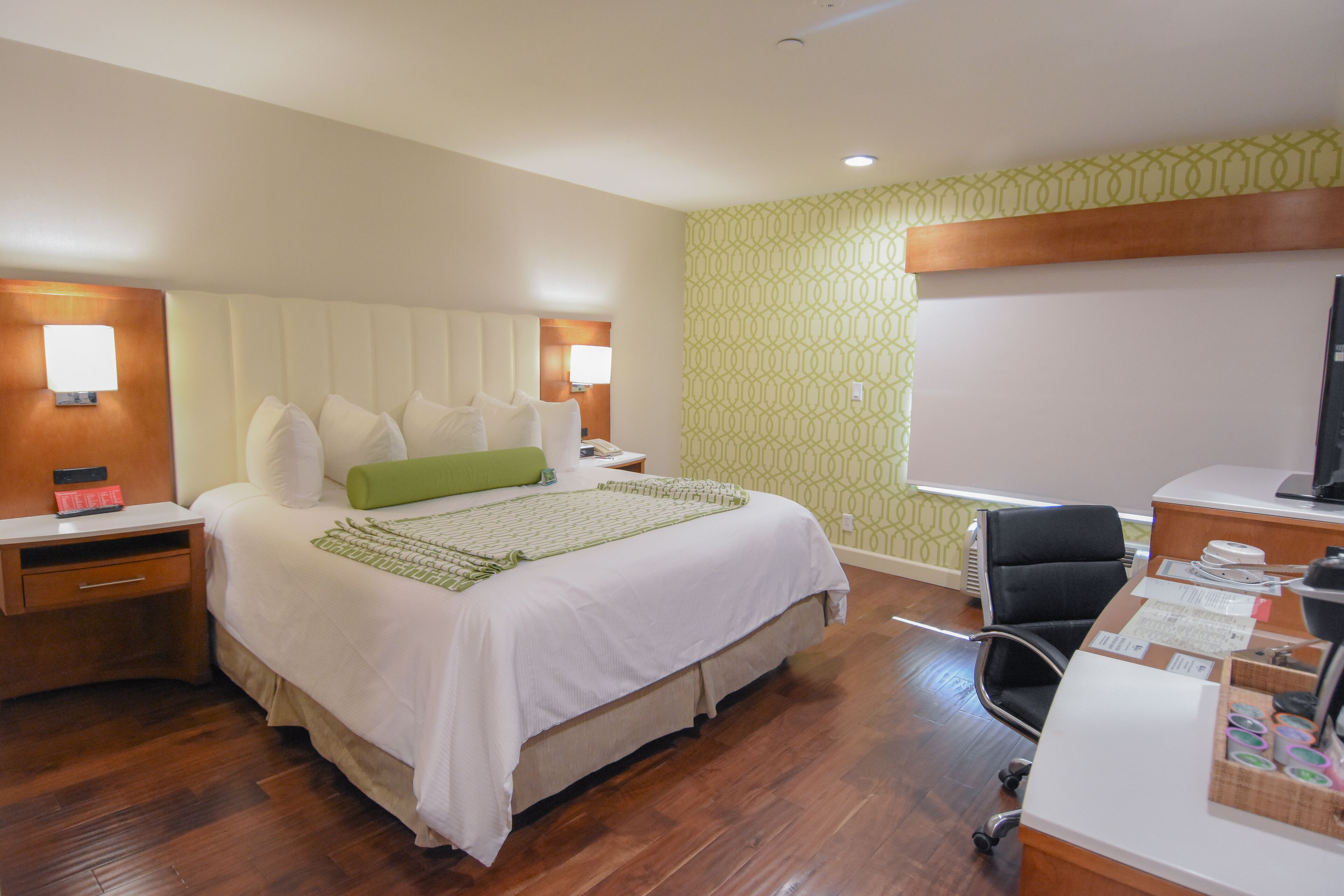 Quarto de hotel com cama, mesas de cabeceira, escrivaninha e televisão.