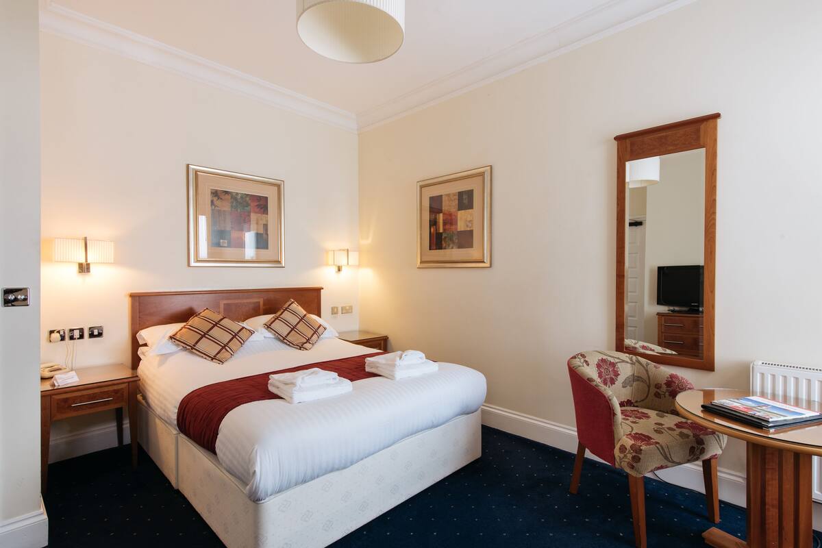 A hotel room with a large bed, bedside lamps, a chair, a table, and artwork on the walls.