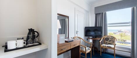 A hotel room with a desk, a television, a chair, and a window with a view.