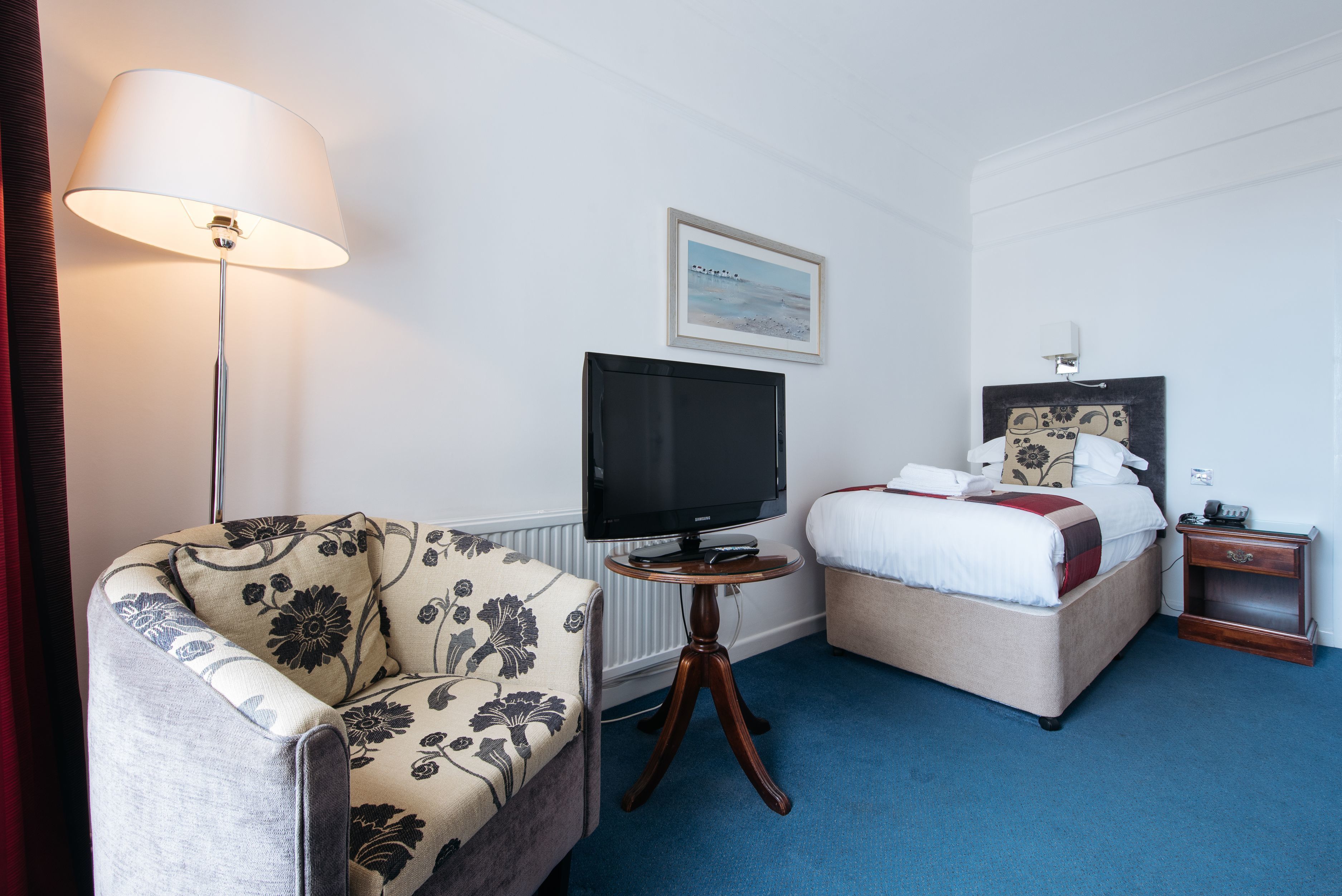 A hotel room with a sofa, a bed, a television on a stand, a bedside table, and a nightstand.