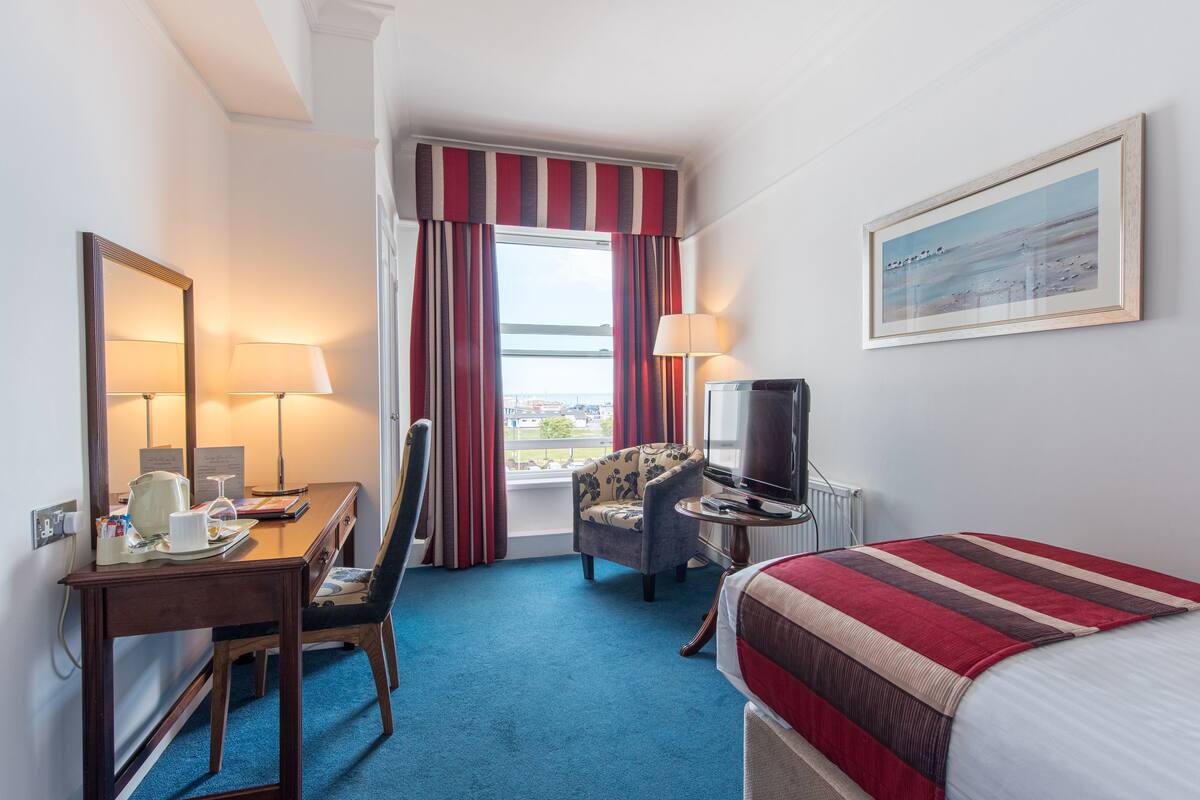 A hotel room with a bed, a desk with a chair, a television, and a window with curtains.