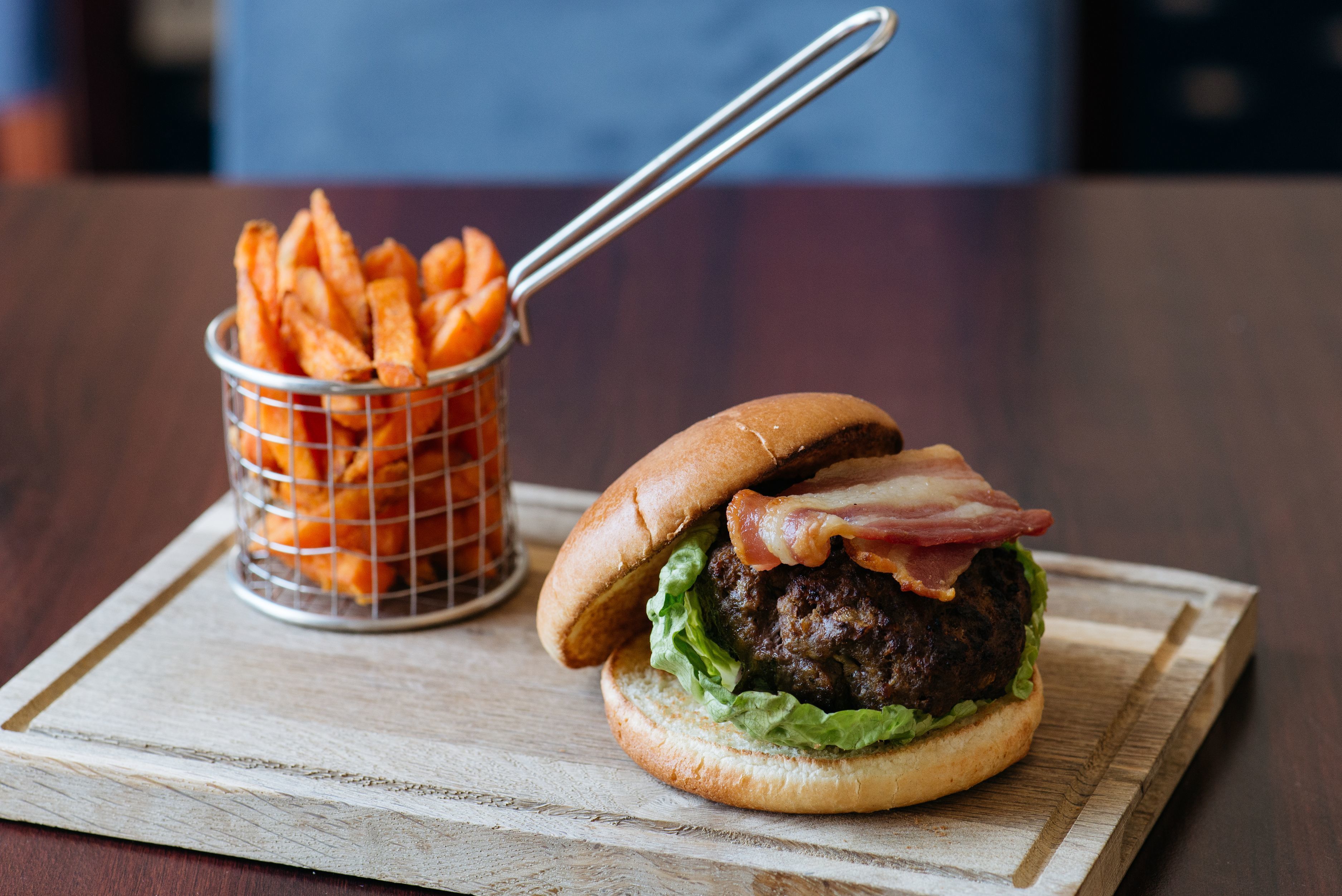 Una hamburguesa con tocino y lechuga, servida con una cesta de papas fritas.