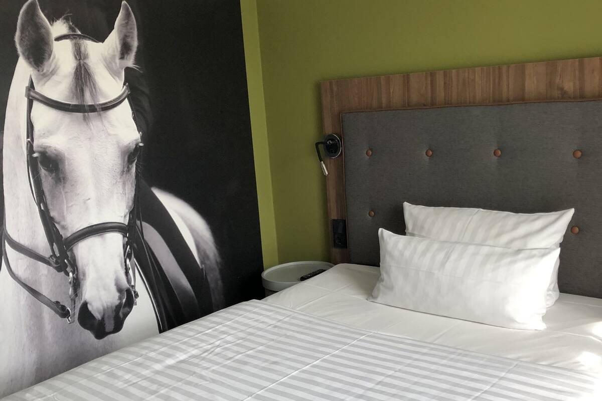 A bedroom with a large bed, a headboard, a wall-mounted TV, and a painting of a horse.