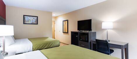 A hotel room with two beds, a desk, a chair, a television, and a lamp.