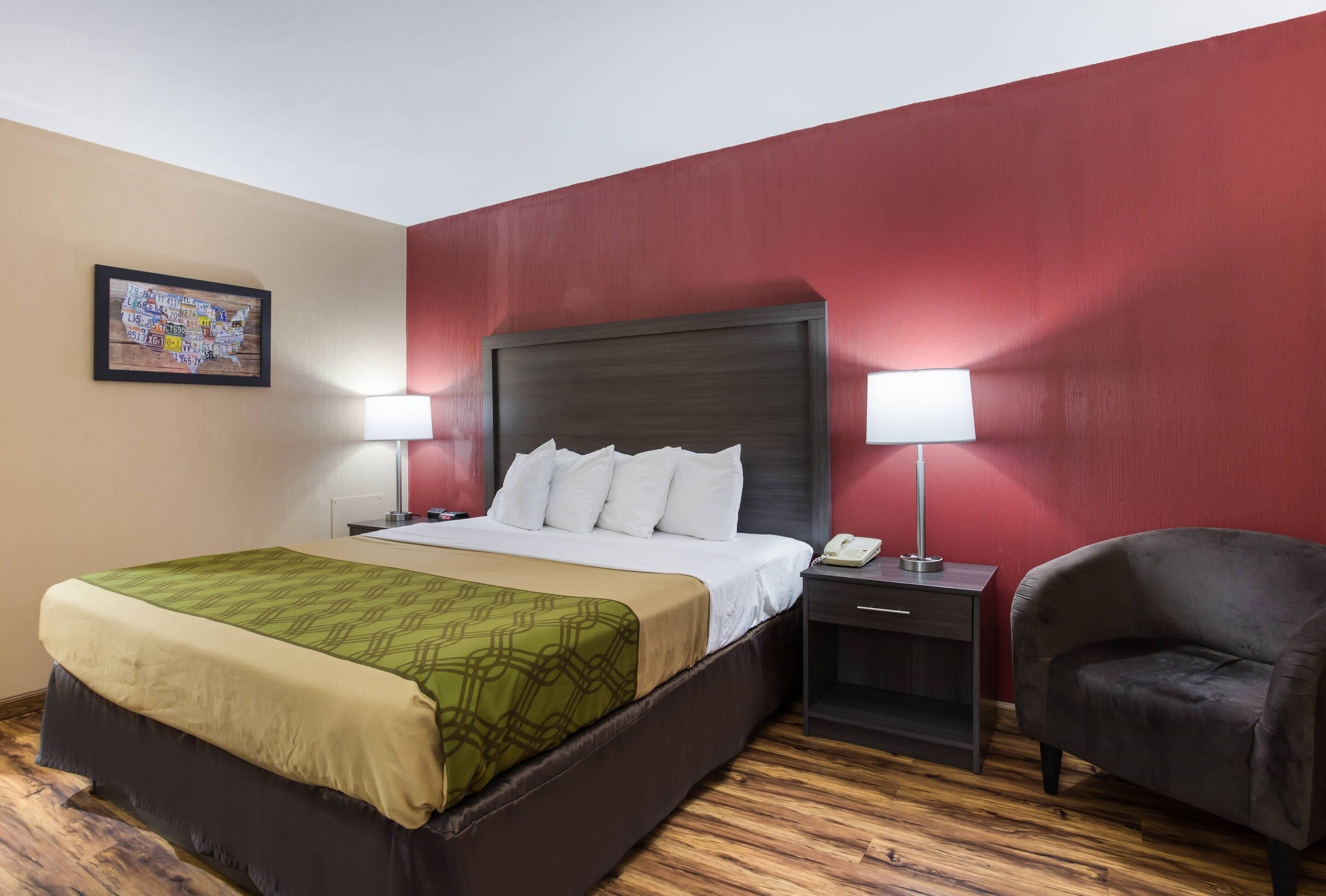 A hotel room with a large bed, two bedside lamps, a nightstand, a chair, and a wall-mounted artwork.