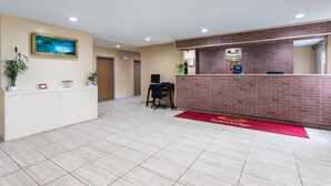 A reception area with a reception desk, a framed picture on the wall, and a red carpet with the hotel logo. - Econo Lodge Painted Post - Corning (Painted Post)