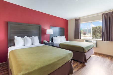 A hotel room with two beds, red walls, and a large window with curtains.