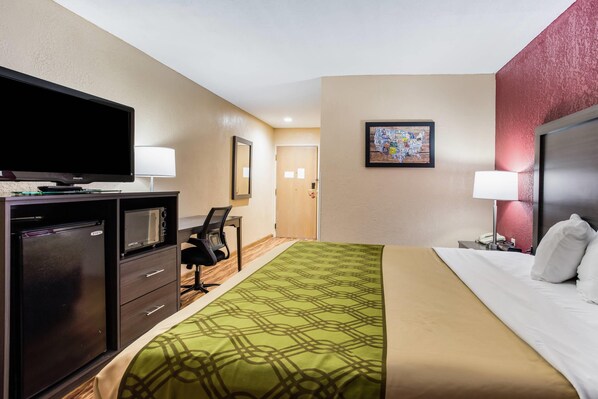 A hotel room with a bed, a desk with a chair, a television, a microwave, and a refrigerator.