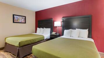 A hotel room with two beds, each with green bedding and white pillows, a bedside table with a lamp, and a framed picture on the wall.