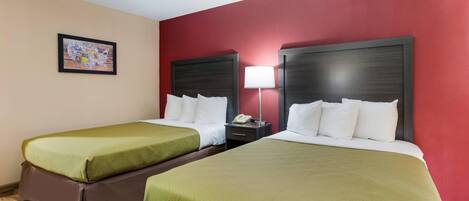 A hotel room with two beds, each with green bedding and white pillows, a bedside table with a lamp, and a framed picture on the wall.