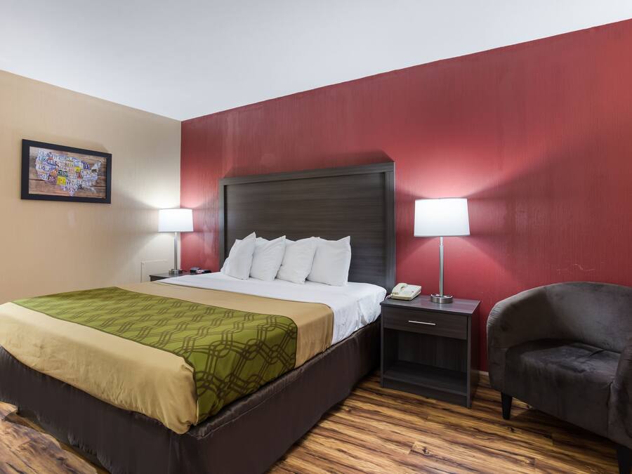 Una habitación de hotel con una cama, dos lámparas de noche, una silla y una mesita de noche.