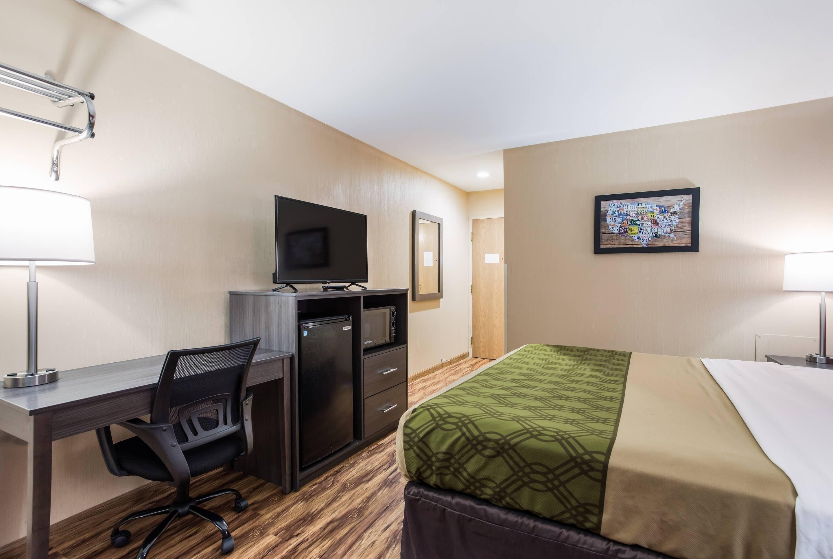 A hotel room with a bed, desk, chair, TV, and a painting on the wall.