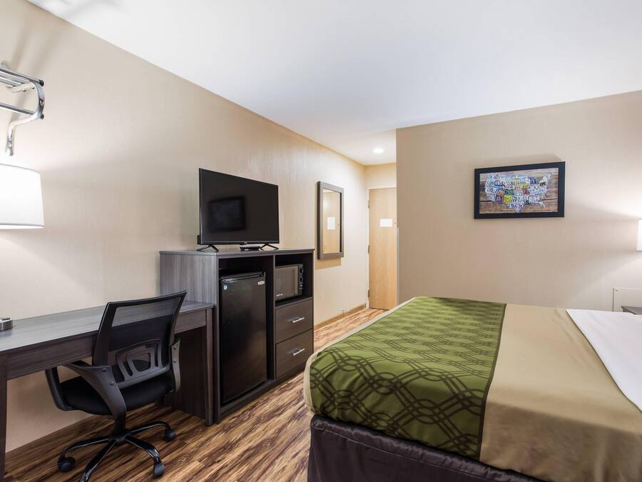A hotel room with a bed, desk, chair, TV, and a painting on the wall.