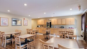 A dining area with wooden tables and chairs, a kitchen with wooden cabinets, and a refrigerator. - Econo Lodge Painted Post - Corning (Painted Post)