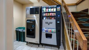 A vending machine with an ice dispenser and a beverage dispenser, located near a staircase with a wooden railing. - Econo Lodge Painted Post - Corning (Painted Post)