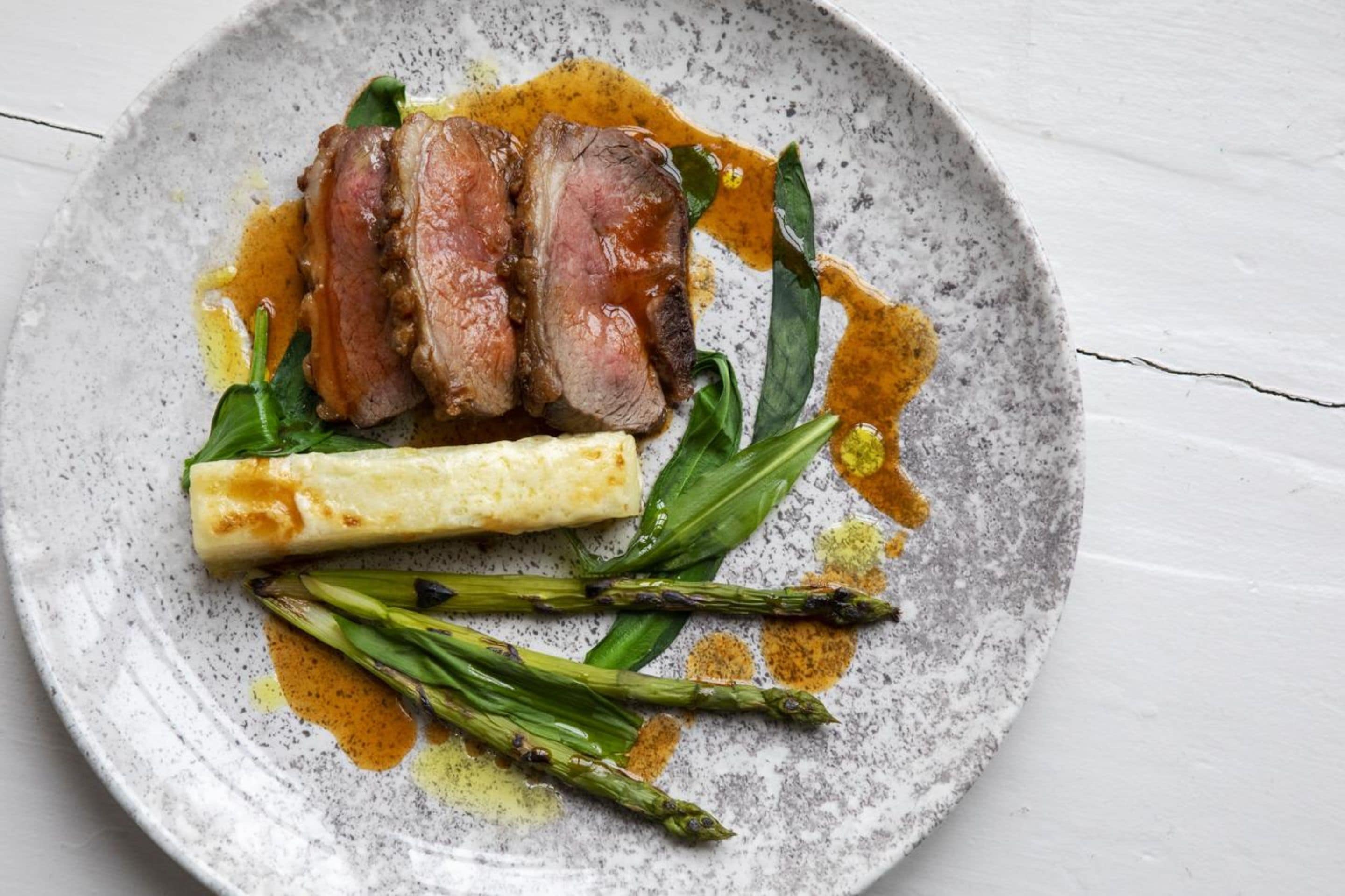 A plate with sliced meat, asparagus, and a rolled vegetable.