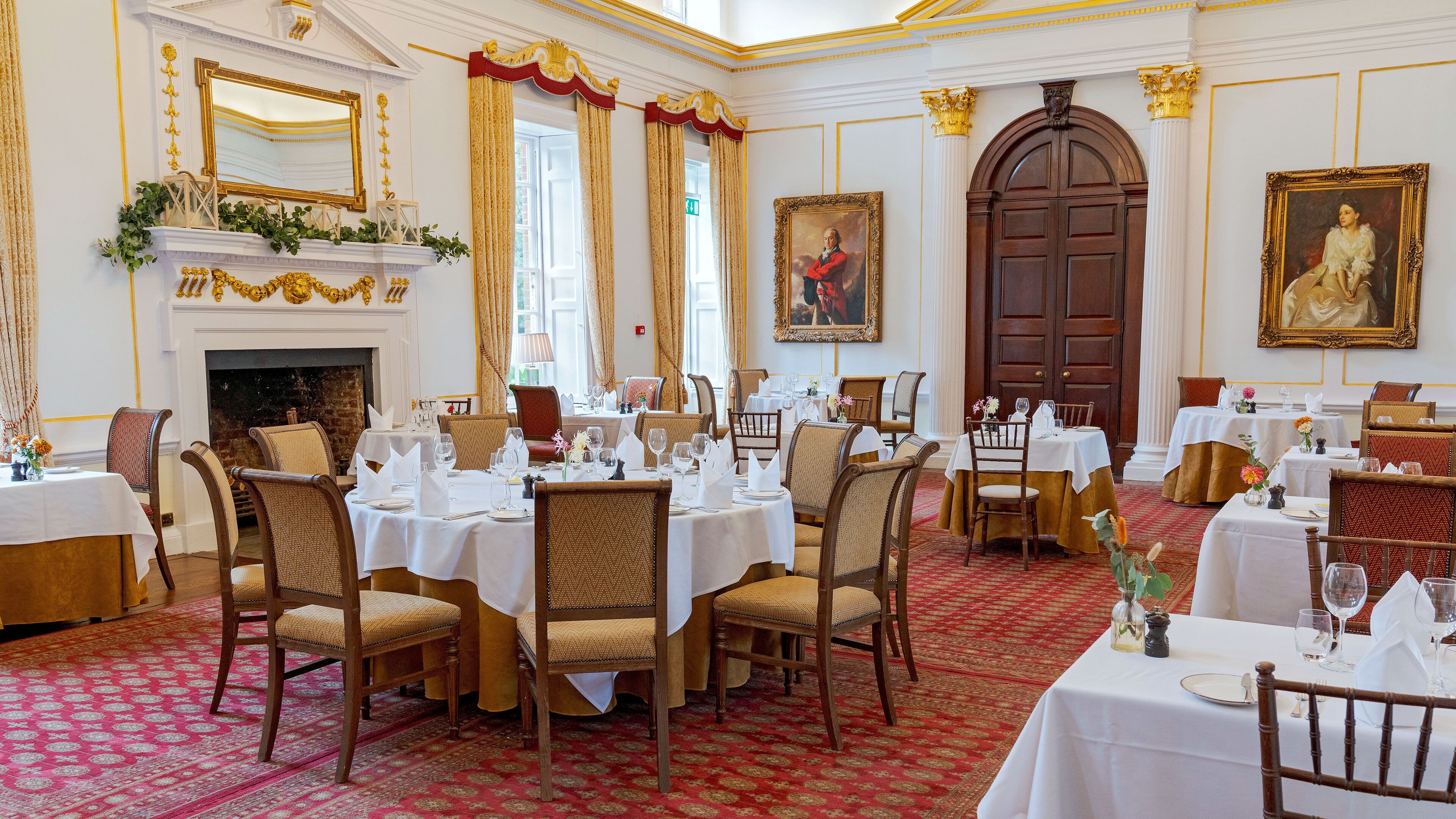 A formal dining room with multiple tables set for service, a fireplace, and classical architectural details.