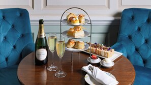 A table with a bottle of champagne, glasses, a tiered dessert stand, and a plate of sandwiches. - Hintlesham Hall Hotel (Ipswich)