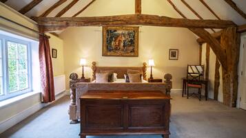 A bedroom with a large bed, a wooden ceiling, a painting on the wall, and a window with curtains.