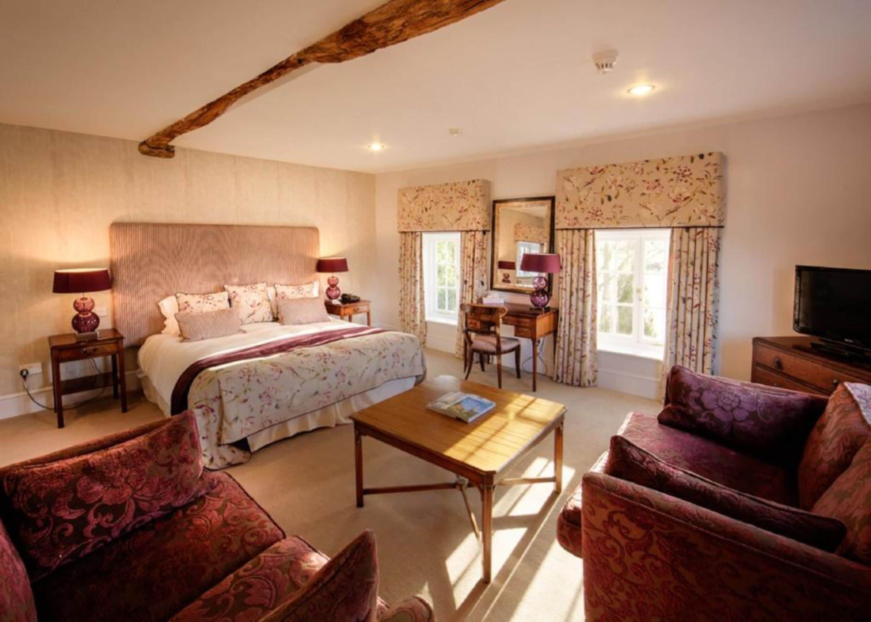 A cozy bedroom with a large bed, a desk, a television, and a seating area with patterned furniture.