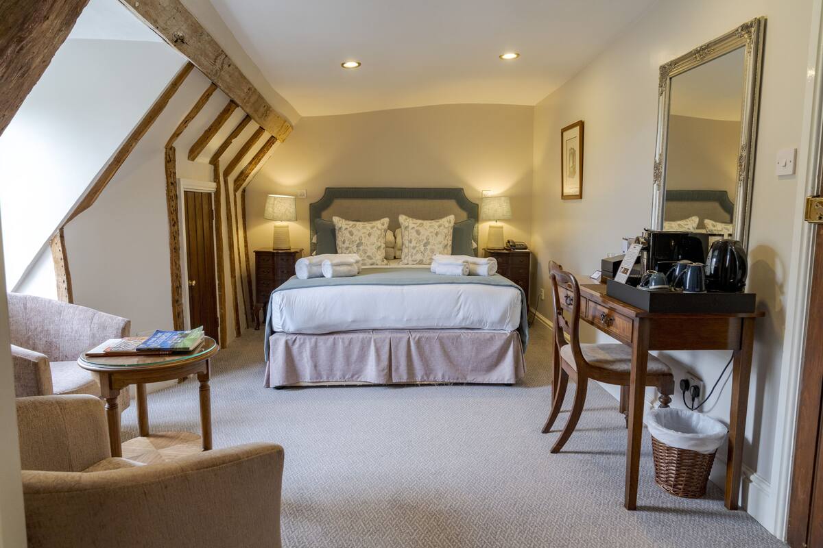 A bedroom with a large bed, two bedside tables with lamps, a desk with a chair, a small table with a book, and a large mirror.