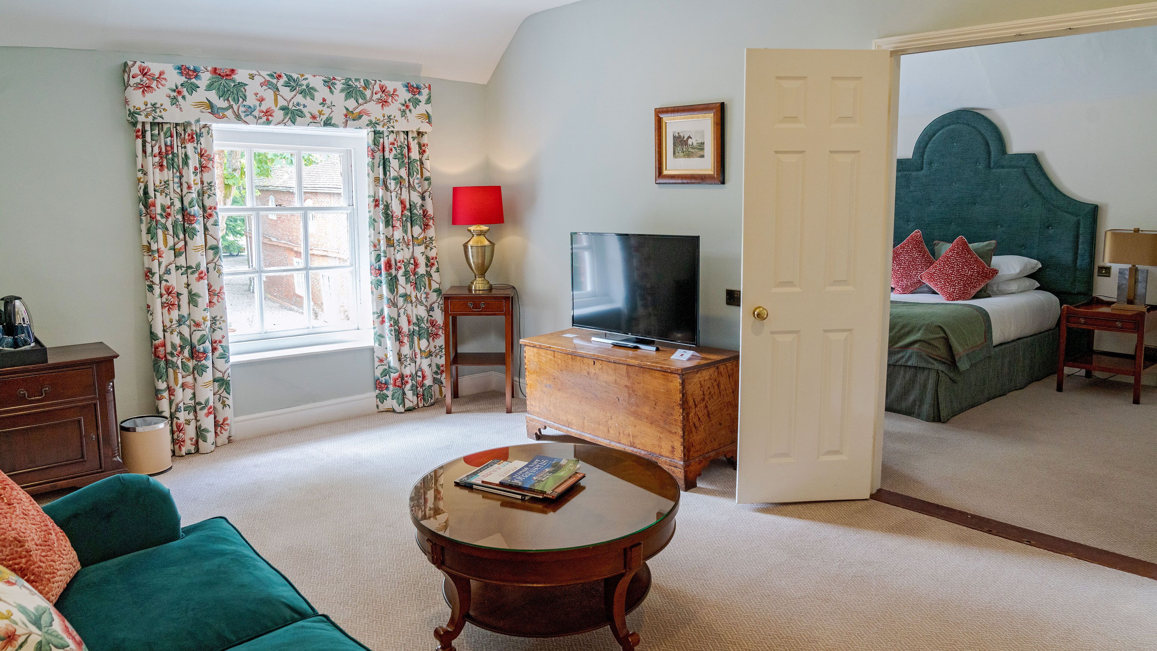 A room with a television, a wooden cabinet, a sofa, a coffee table, and a bed with green bedding.