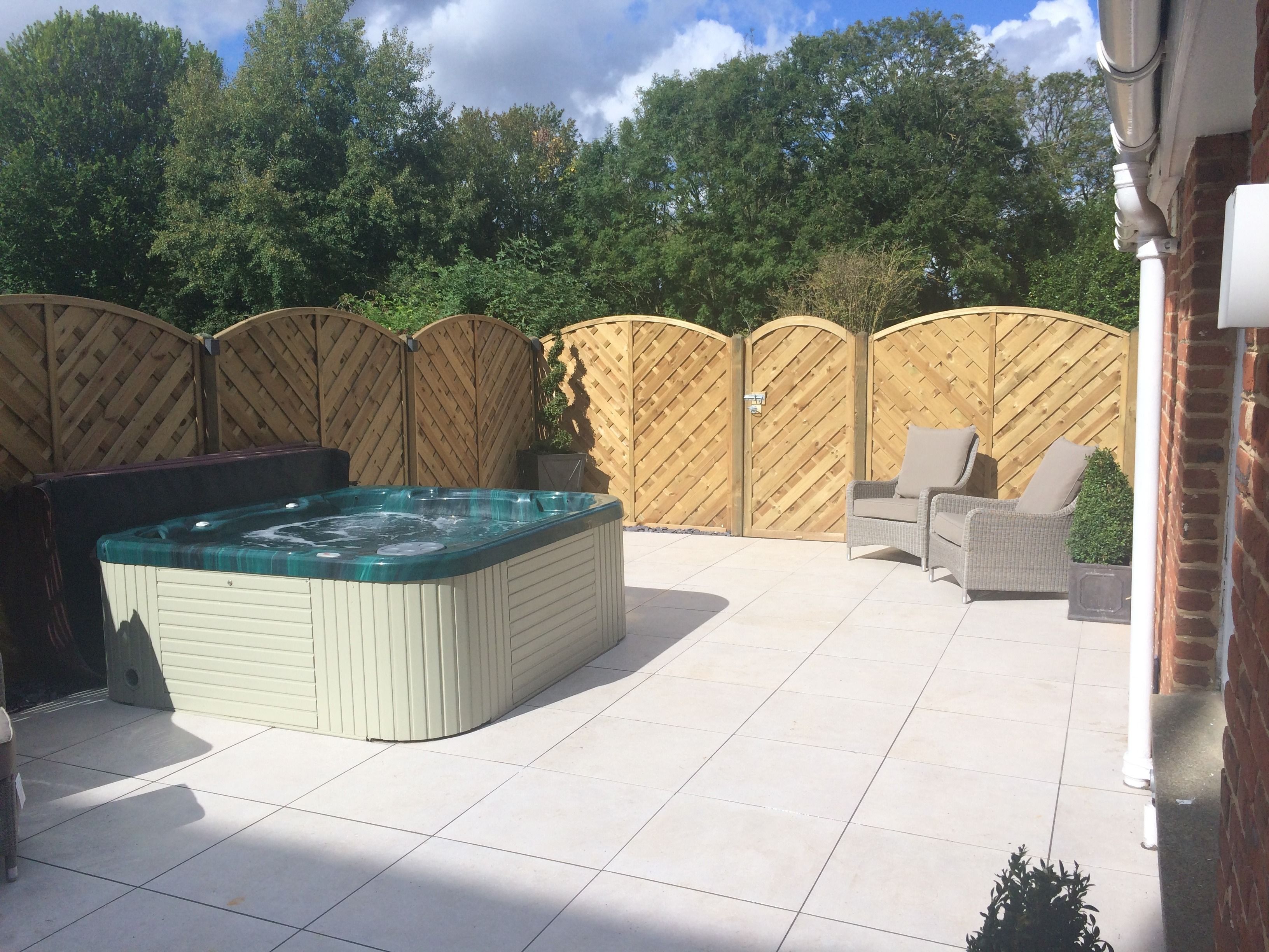 Un jacuzzi en un patio trasero con un patio de baldosas, una silla de mimbre y una valla de madera.