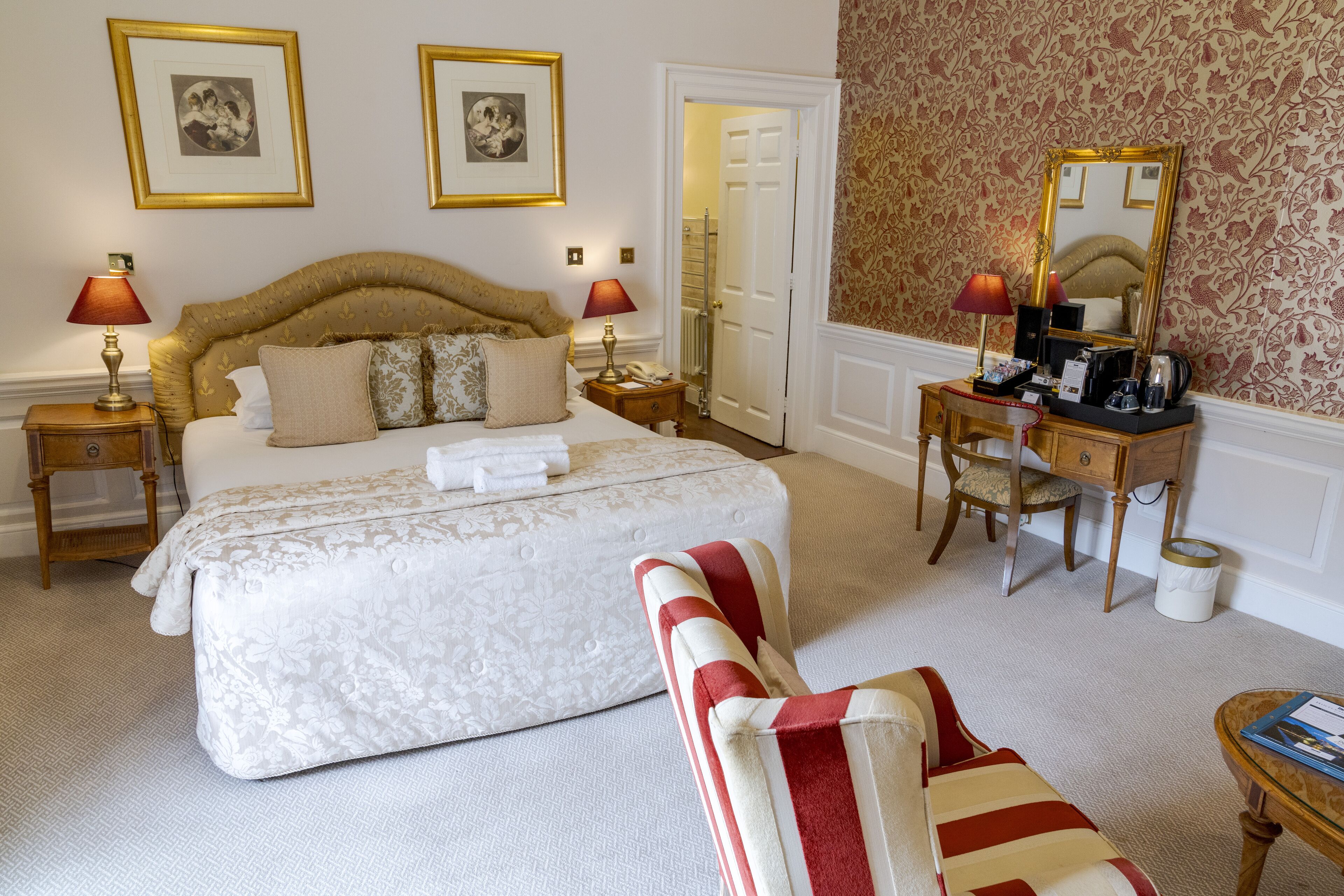 A hotel room with a large bed, two bedside tables with lamps, a chair, a desk with a mirror, and a small table with a book.