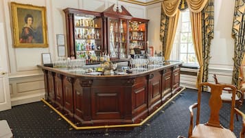 A bar area with a wooden bar counter, shelves with bottles, and glasses.
