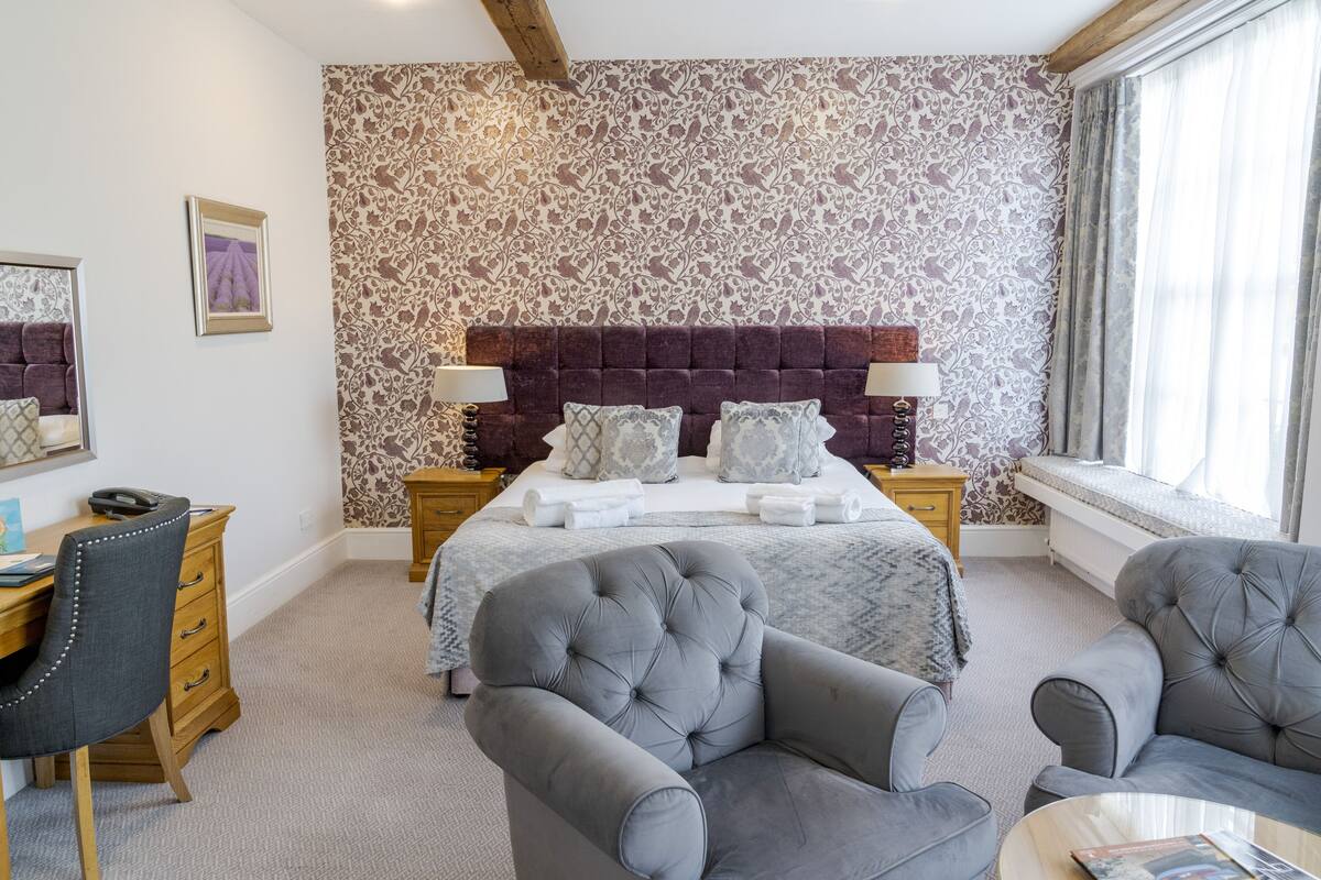 A bedroom with a large bed, two bedside tables, a desk, and two armchairs.