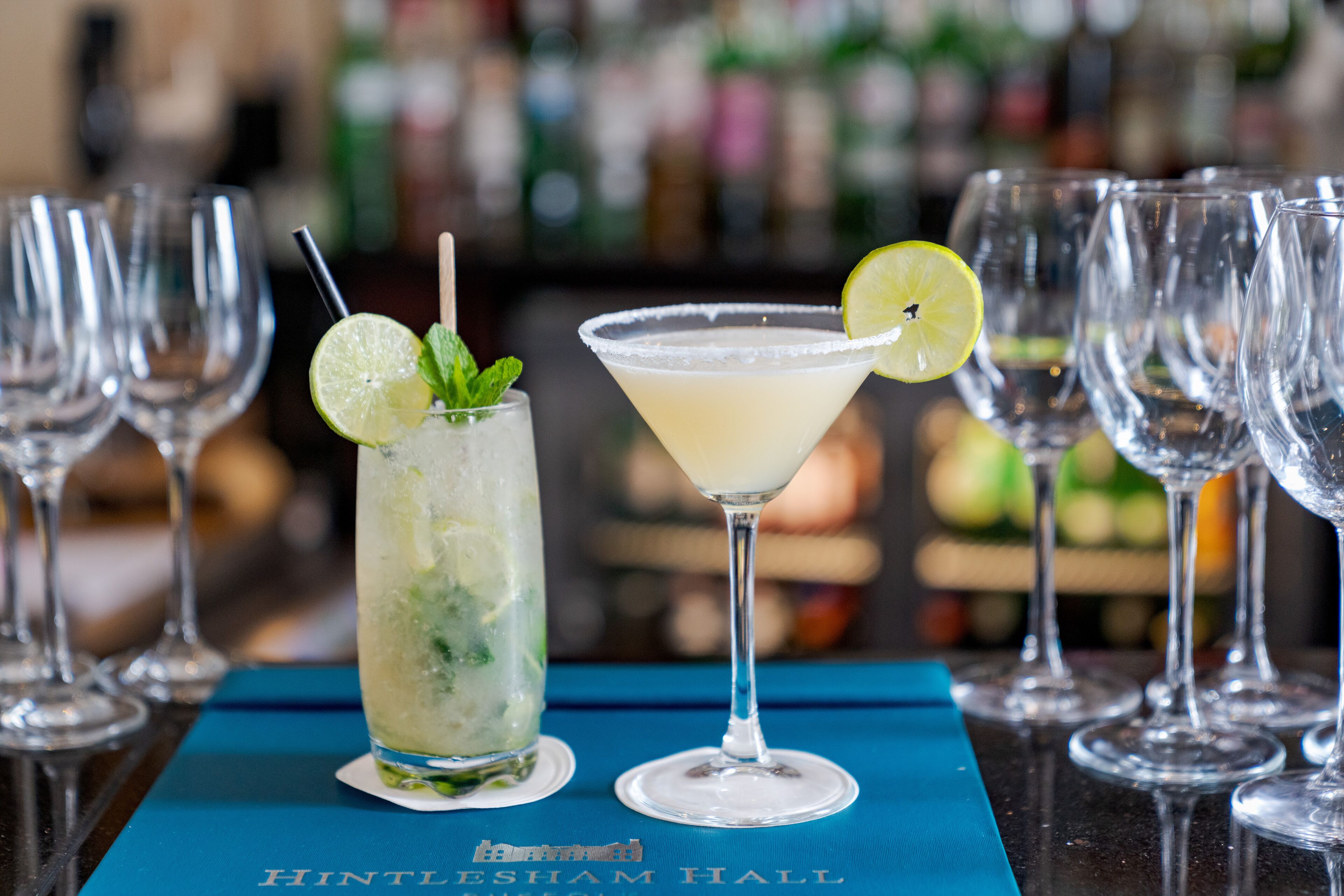 A bar setting with two cocktails, a lime garnish, and mint leaves.