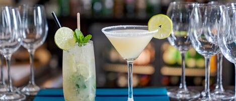 A bar setting with two cocktails, a lime garnish, and mint leaves.