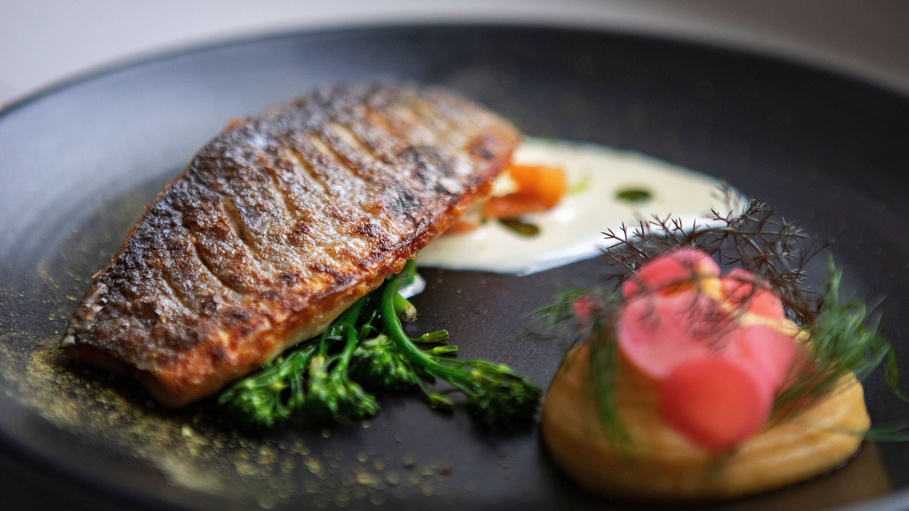 Une assiette contenant un poisson grillé, des légumes verts et une petite portion de sauce.