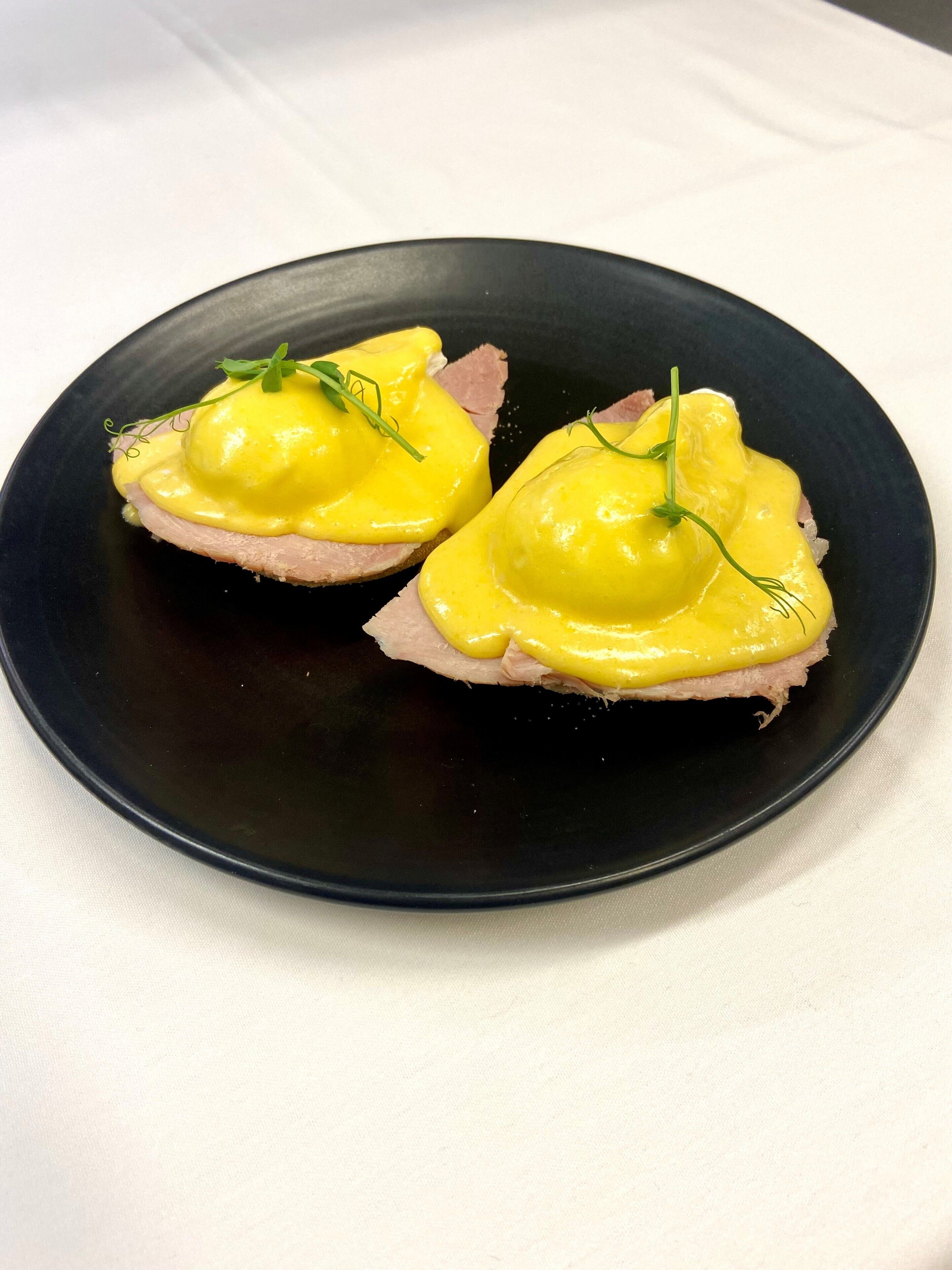 Une assiette noire contenant deux portions de nourriture, chacune recouverte d’une sauce jaune et décorée de feuilles vertes.