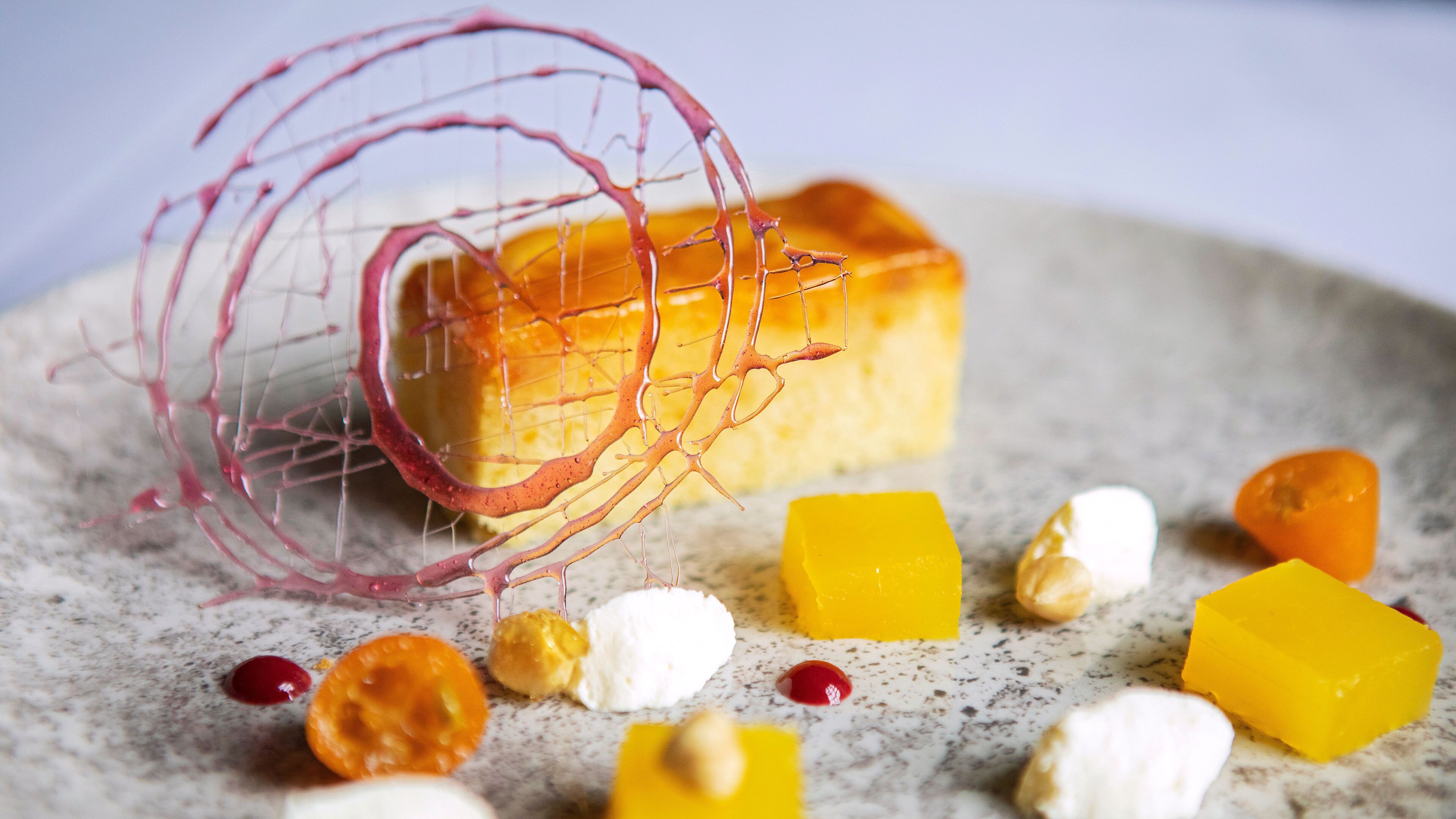 Un postre con una escultura de alambre, cubos amarillos y caramelos pequeños y redondos sobre una superficie moteada.