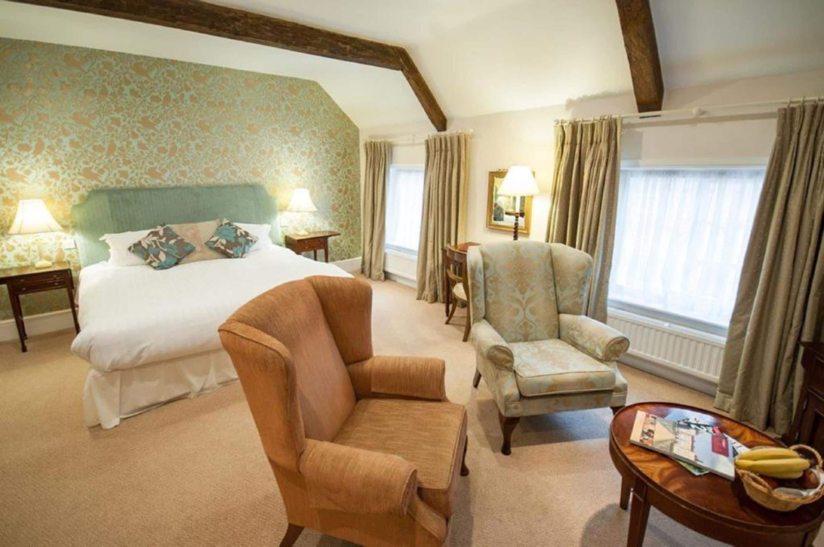 A hotel room with a large bed, two armchairs, a small table, and a window with curtains.