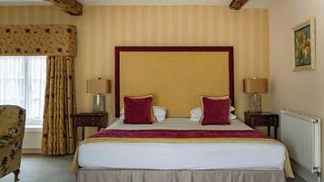 A hotel room with a large bed, two bedside tables, a window with curtains, a radiator, and a painting on the wall.