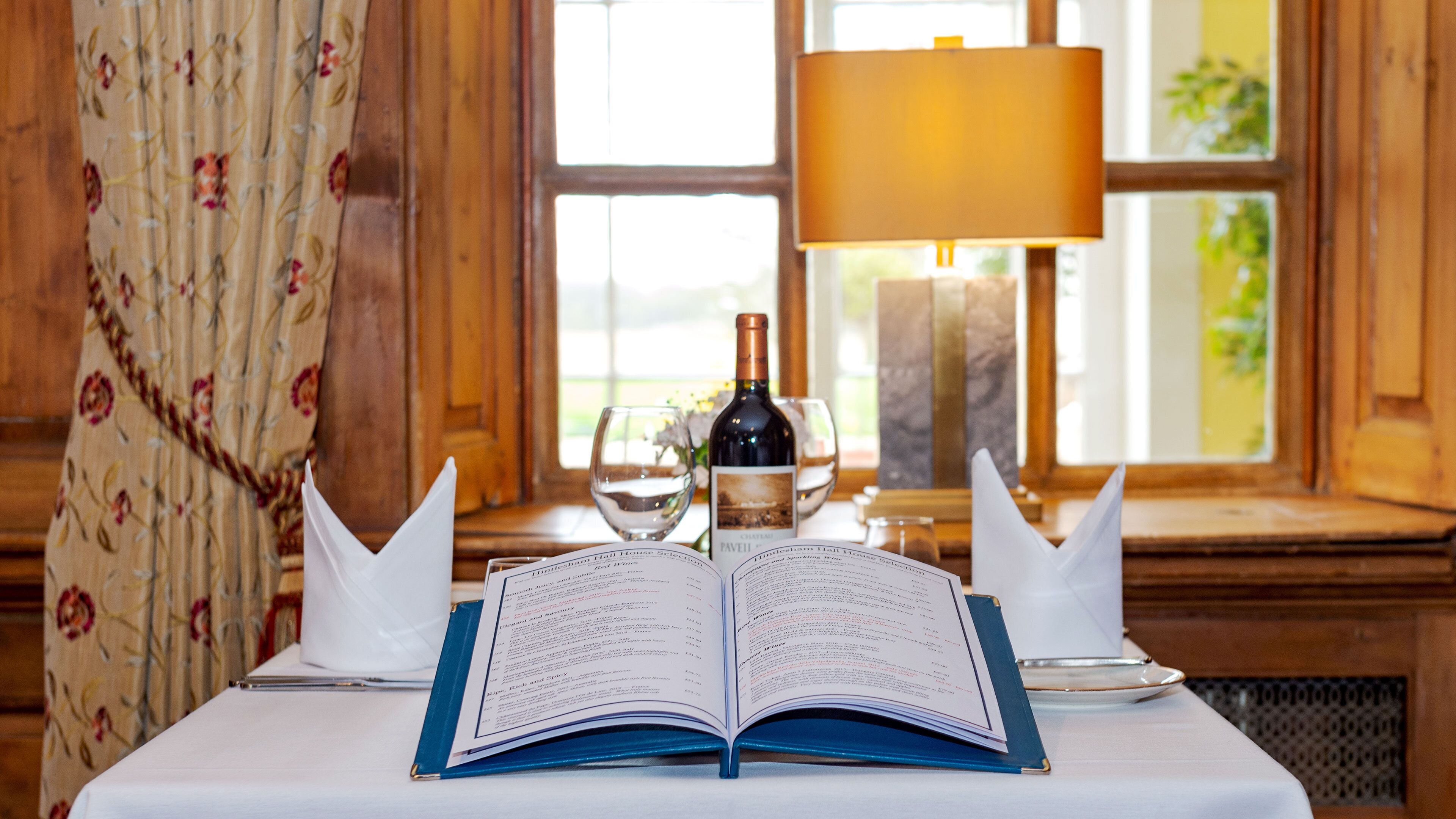 Une table avec un menu ouvert, une bouteille de vin et deux verres.
