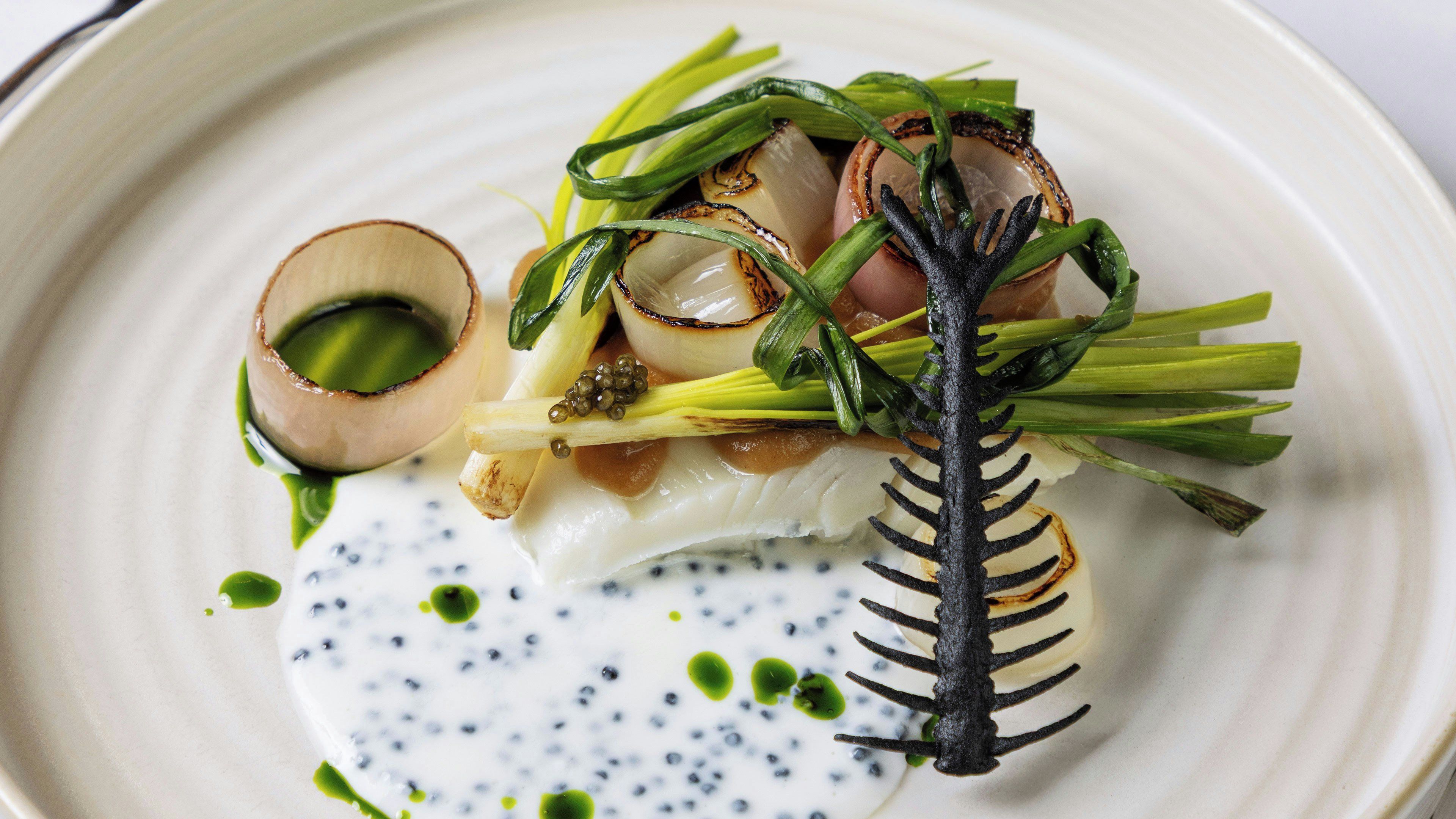 A plate of food with a decorative black structure, possibly a plant, and a small bowl of sauce.