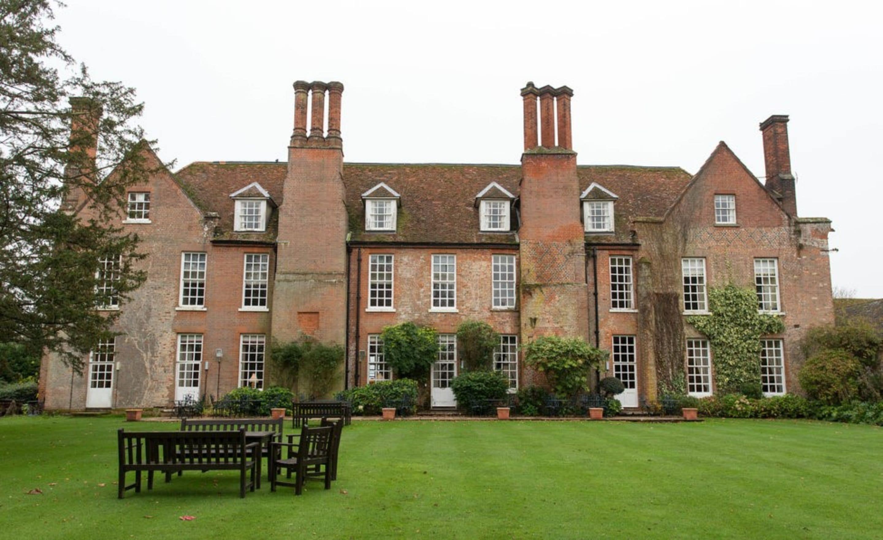 A large, historic brick building with multiple chimneys, a well-maintained lawn, and outdoor seating.
