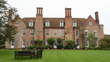 A large, historic brick building with multiple chimneys, a well-maintained lawn, and outdoor seating.