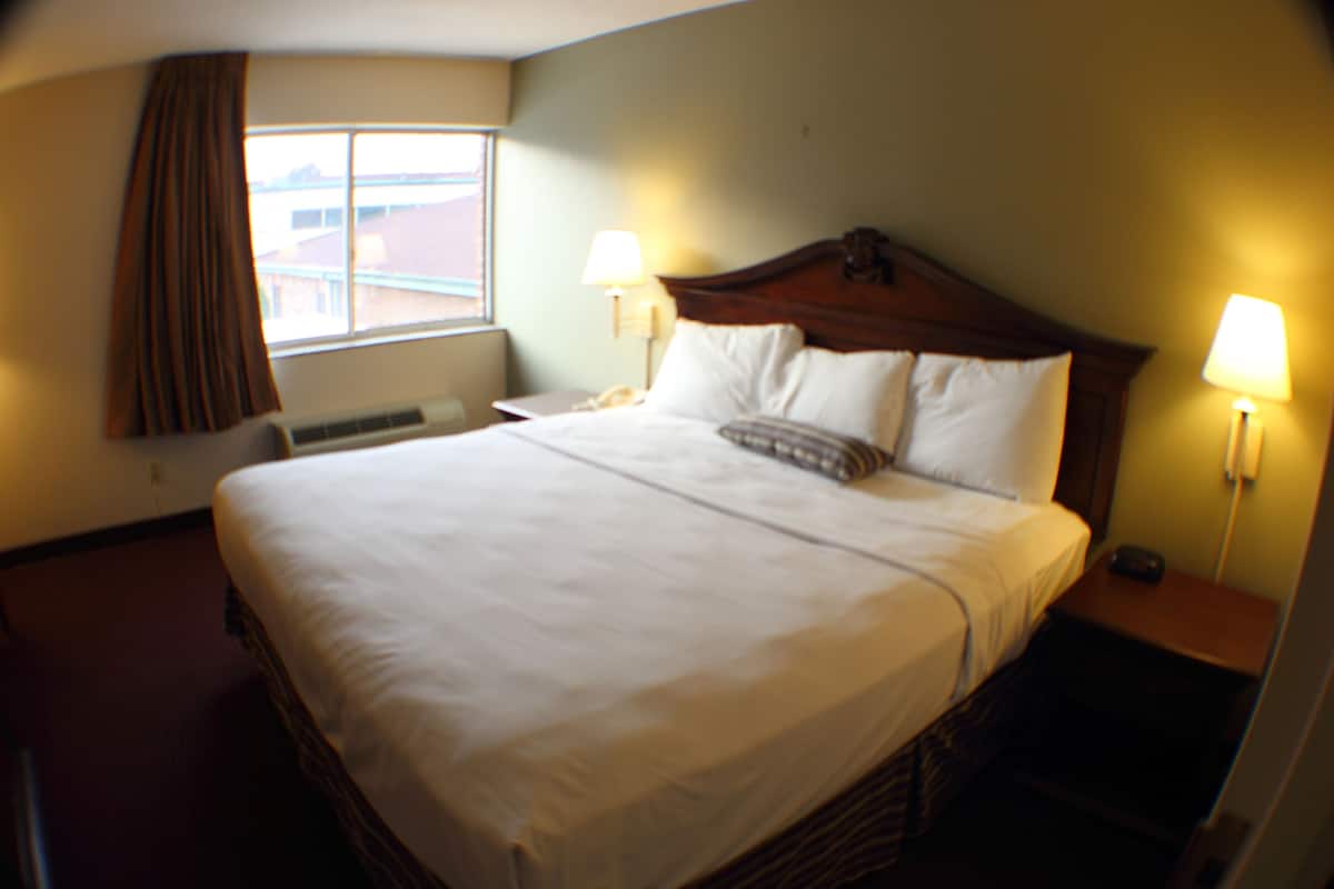 A hotel room with a large bed, two bedside lamps, a window with curtains, and a thermostat on the wall.