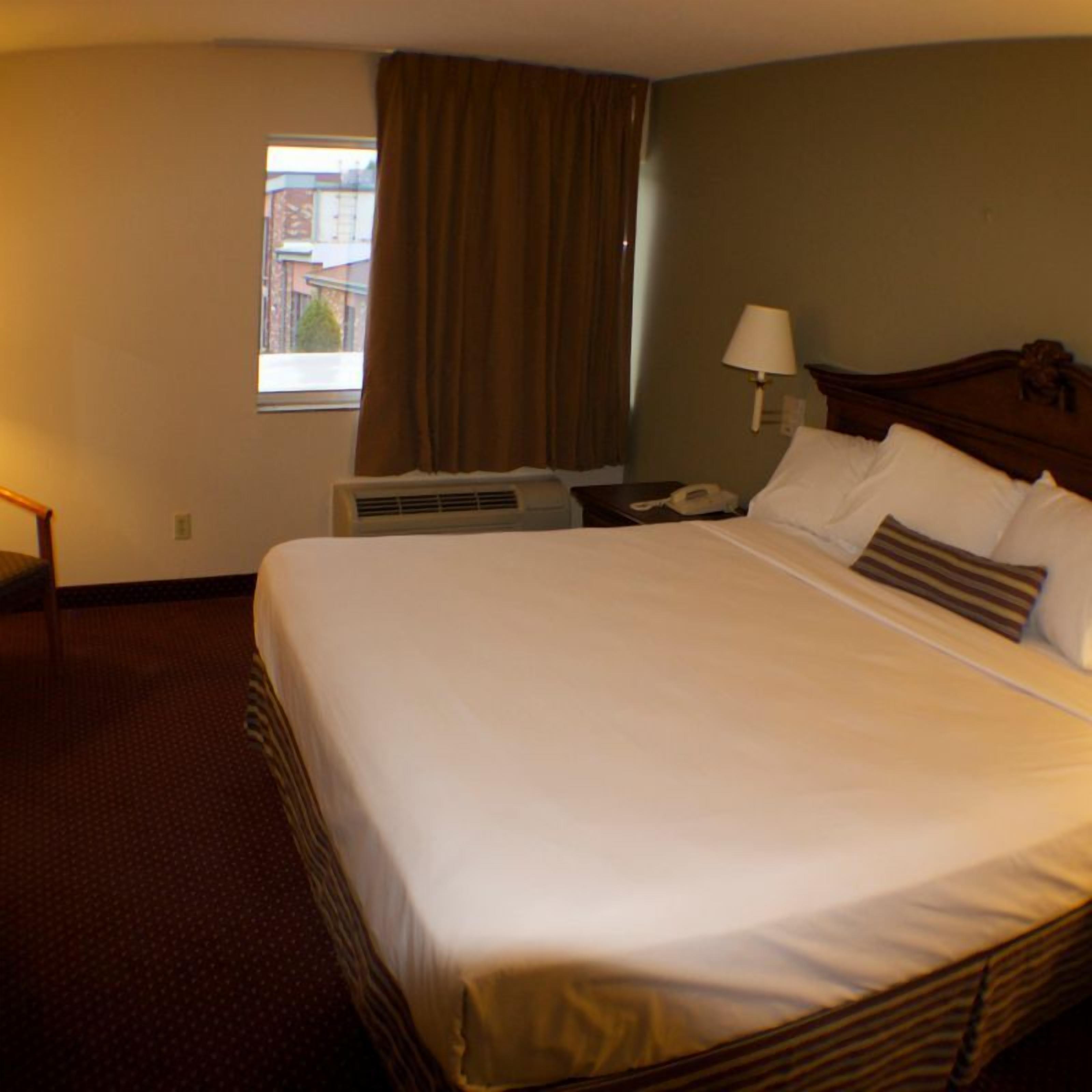 Una habitación de hotel con una cama grande, una mesita de noche con lámpara, un equipo de aire acondicionado y un ventanal con cortinas.