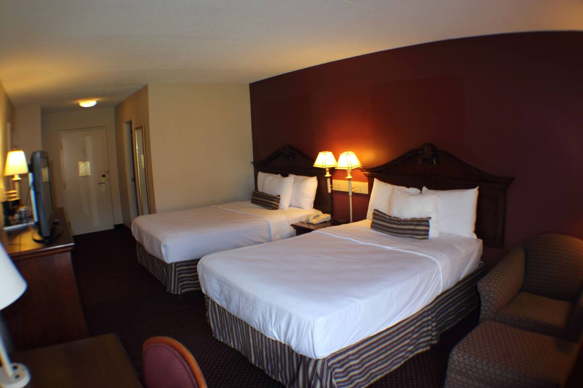 A hotel room with two beds, a desk, and a chair.